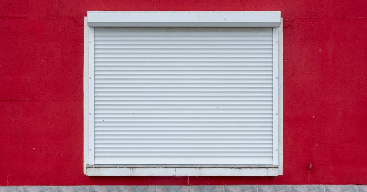 Vue extérieure minimaliste d'un volet roulant blanc sur un mur rouge vif.