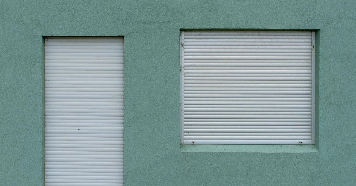 Une composition minimaliste de deux volets blancs sur un mur vert, mettant en avant la simplicité et le design urbain.