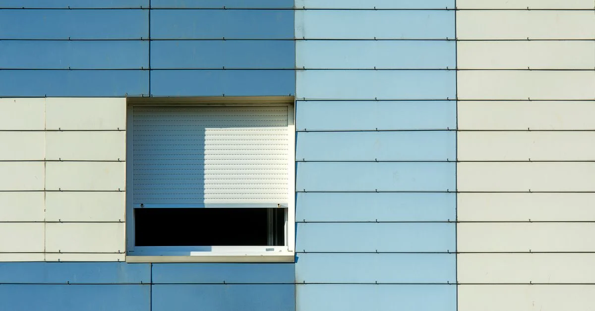 Détail architectural minimaliste d'une façade bleue et beige avec un volet de fenêtre.