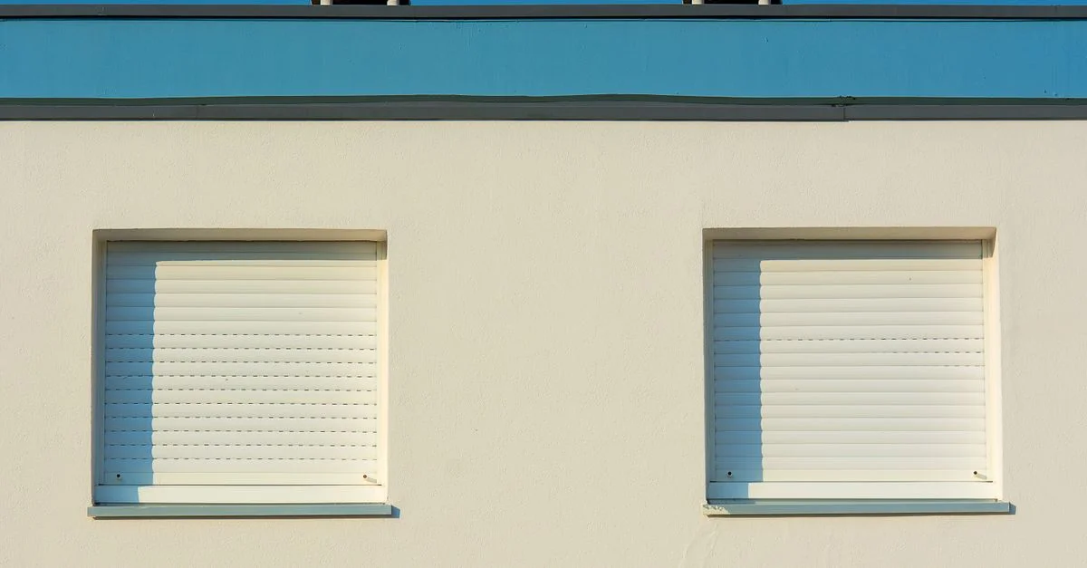 Deux fenêtres à volets fermés sur la façade d'un bâtiment moderne sous un ciel dégagé.