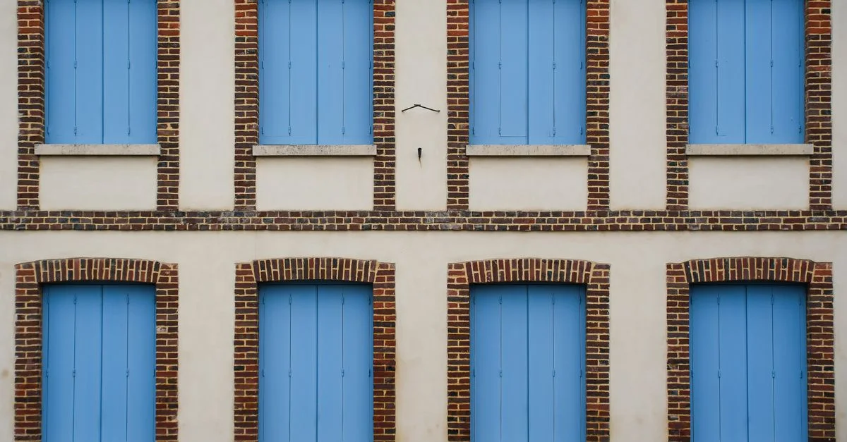 Une façade minimaliste caractérisée par des rangées symétriques de fenêtres à volets bleus et des accents de brique.