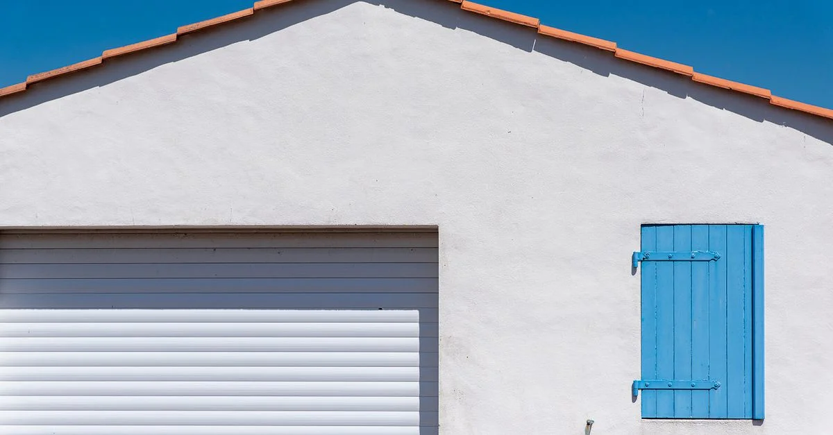 Mur blanc avec un volet bleu sous un ciel bleu limpide, illustrant une architecture minimaliste.